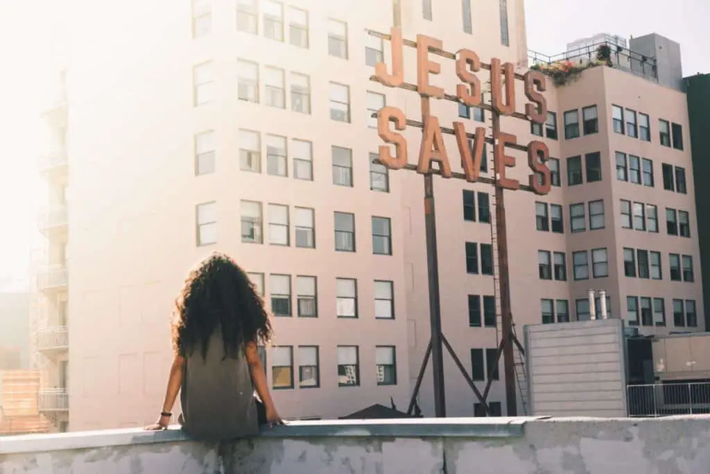 Woman sitting on a roof with a sign that says: Jesus Saves
